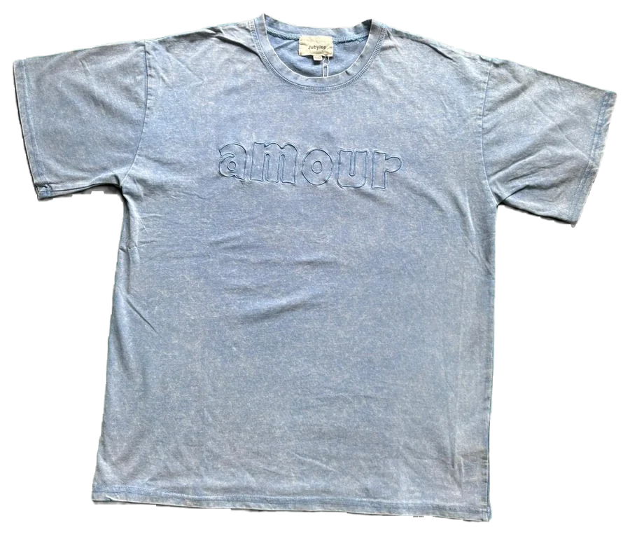 Un t-shirt bleu délavé posé à plat, photographié au téléphone sur un drap vert